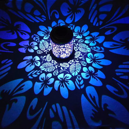 Lantern with tropical flower design creating a pattern of blue light on the surface around it.