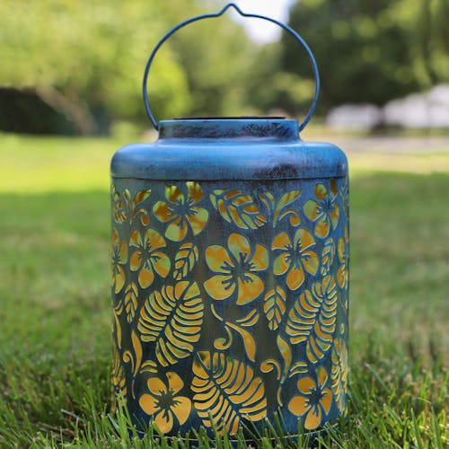 Blue Solar Lantern with tropical flower design standing on grass.