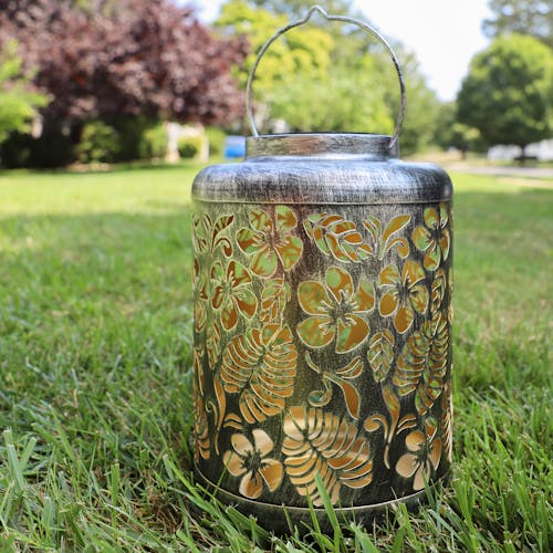 Silver Solar Lantern with tropical flower design standing on grass.