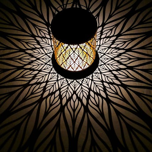Lantern with diamond leaf design creating a white pattern on the surface around it.