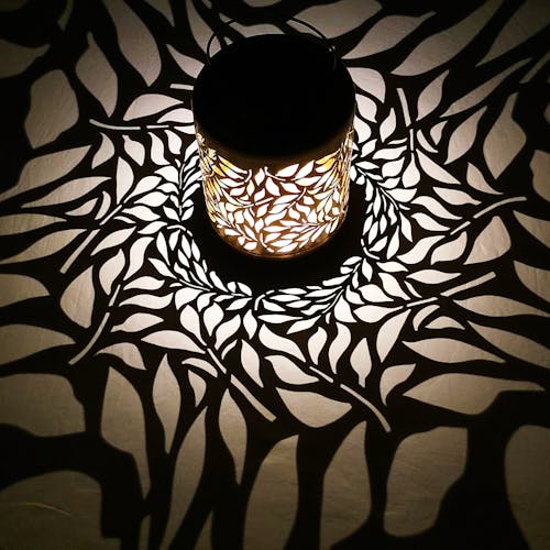 Lantern with olive leaf design creating a white pattern on the surface around it.