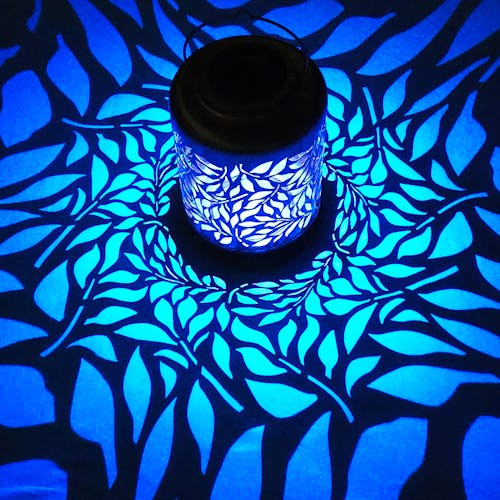 Lantern with olive leaf design creating a blue pattern on the surface around it.