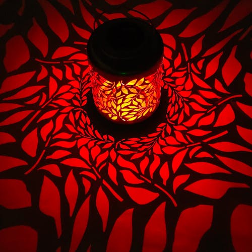 Lantern with olive leaf design creating a red pattern on the surface around it.