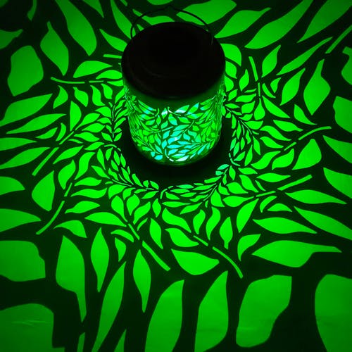 Lantern with olive leaf design creating a green pattern on the surface around it.