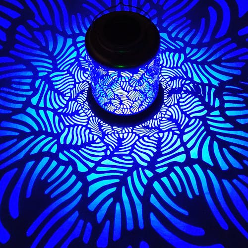 Lantern with banana leaf design creating a blue pattern on the surface around it.