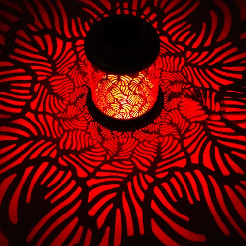 Lantern with banana leaf design creating a red pattern on the surface around it.