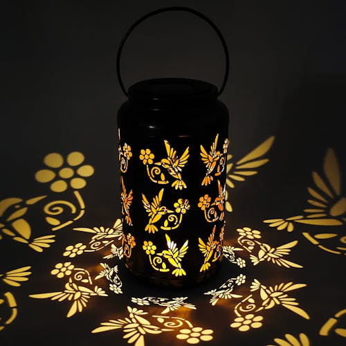 Lantern with humming bird design creating a light pattern on the surface around it.