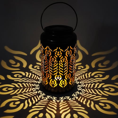 Lantern with phoenix feather design creating a light pattern on the surface around it.