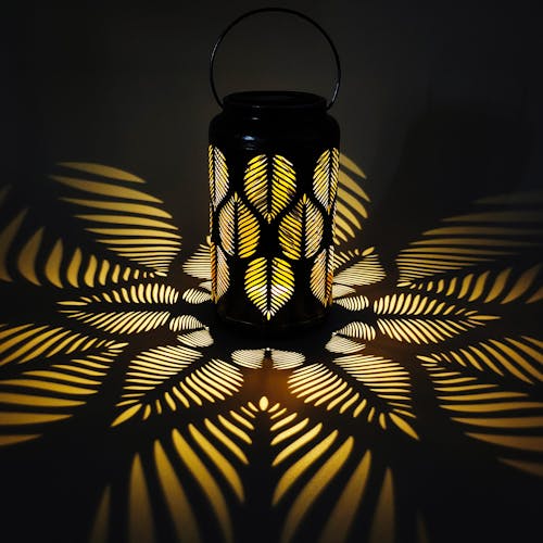 Lantern with tropical leaf design creating a light pattern on the surface around it.