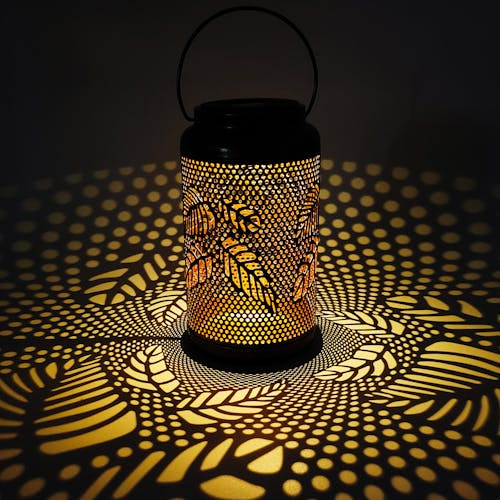 Lantern with berry leaf design creating a light pattern on the surface around it.
