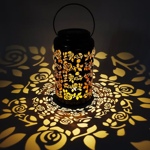 Lantern with rose design creating a light pattern on the surface around it.