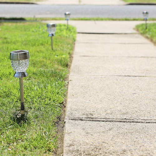14-inch Solar LED Pathway Light staked in the ground next to a walkway with more in the background.