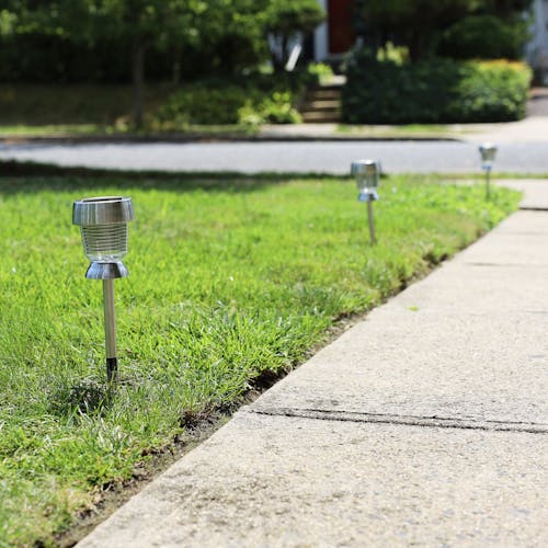 3 solar powered led lights staked in the ground along the side of a pathway.