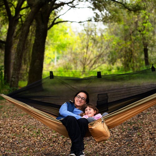 Woman and young girl sitting in the Bliss Hammocks 54-inch wide Desert Storm Camping Hammock with mosquito net.