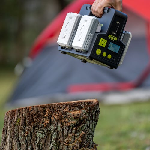 Person placing the Sun Joe 24-Volt Cordless Hot-Swap Powered Inverter Generator Power Station on a tree stump with batteries charging.