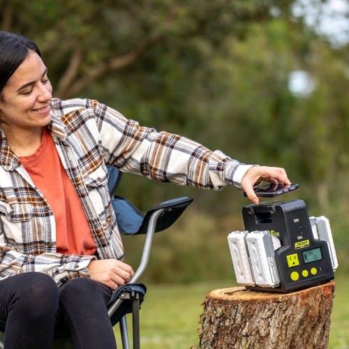 Woman placing her phone on the Sun Joe 24-Volt Cordless Hot-Swap Powered Inverter Generator Power Station to charge it.