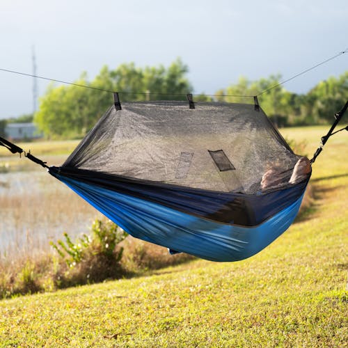 Person relaxing outside in the sun in the Bliss Hammocks 54-inch wide Royal Blue Camping Hammock with mosquito net.