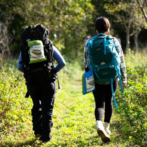 2 people walking along a trail with the Bliss Hammock in a bag attached to their backpacks.