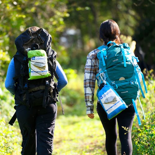 2 people walking along a trail with the Bliss Hammock in a Bag attached to their backpacks.