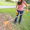 Woman using the ErgieSystems 54-inch Steel Shaft Strain Reducing Steel Leaf Rake with 24 tines to rake leaves.