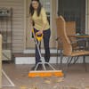 Woman using the ErgieSystems 24-inch wide Steel Shaft Strain Reducing Indoor/Outdoor Push Broom to weep leaves off a patio.