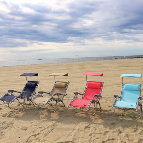 4 beach recliners on the sand on a sunny day, each a different color: navy, taupe, coral, and sea glass.