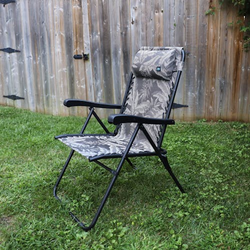 Angled view of the 26-inch Platinum Fern Reclining Sling Chair on a lawn next to a fence.