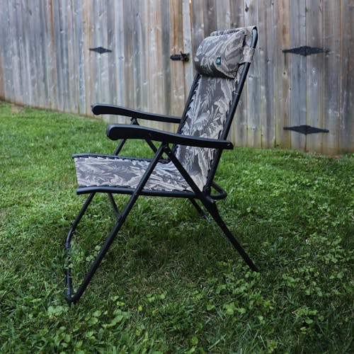 Side view of the 26-inch Platinum Fern Reclining Sling Chair on a lawn next to a fence.