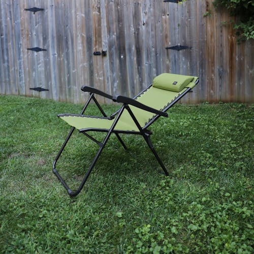 Angled view of a reclined 26-inch Sage Green Reclining Sling Chair on a lawn next to a fence.