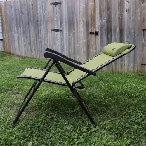 Side view of a reclined 26-inch Sage Green Reclining Sling Chair on a lawn next to a fence.