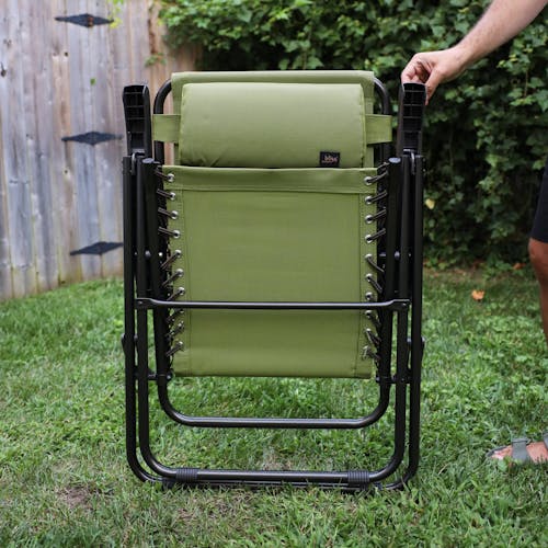 Person holding up a folded 26-inch Sage Green Reclining Sling Chair on a lawn.