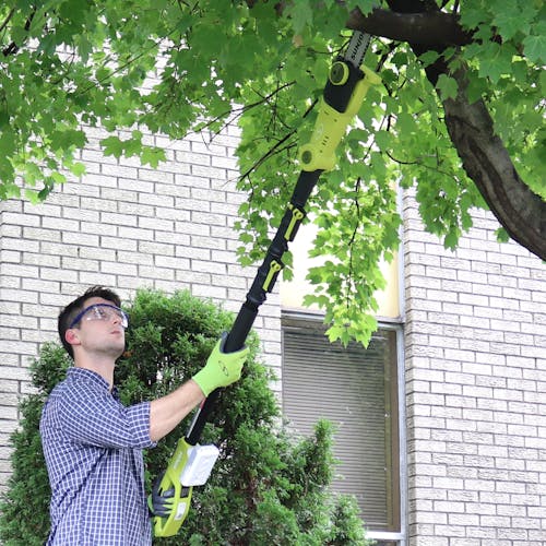 Man using the pole saw attachment on the Sun Joe 24-Volt Cordless 3-in-1 yard solution kit to cut a branch off a tree.