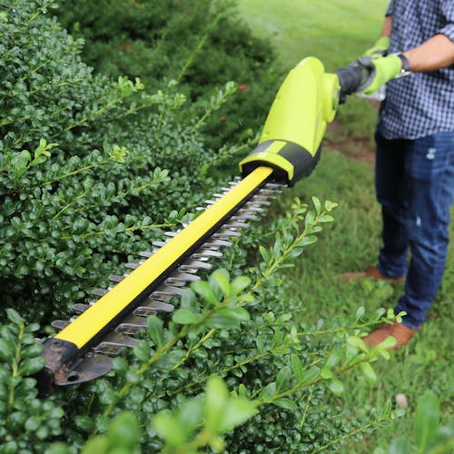 Hedge trimmer attachment being used to trim a bush.