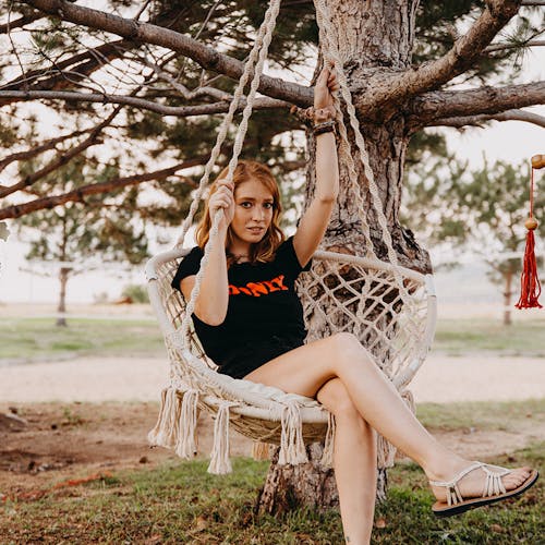 Girl sitting in the Bliss Hammocks 31.5-inch Wide White Macramé Swing Chair hanging from a tree.
