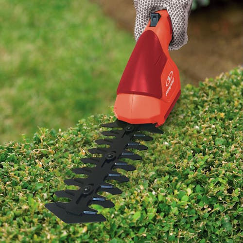 Sun Joe 2-in-1 Cordless red-colored Grass Shear and Hedger trimming a bush.
