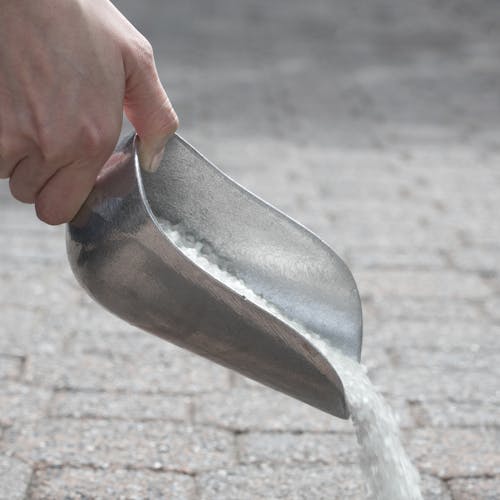 Pure Sodium Rock Salt Ice Melter being poured from the scooper.