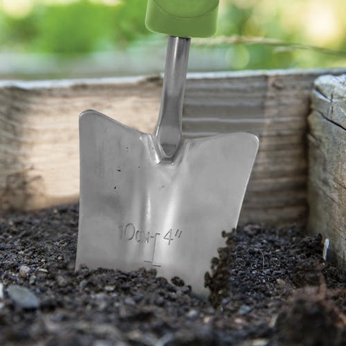 Close-up of the Martha Stewart Stainless Steel Transplanter dug in soil.
