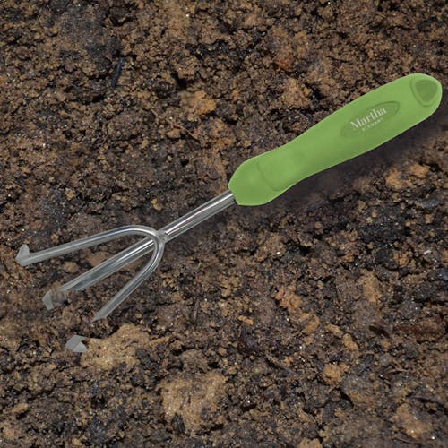 Martha Stewart 3-pronged tainless Steel Hand Cultivator digging through soil.