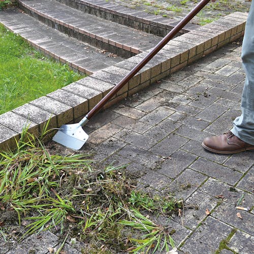Nisaku Zassou Burush Obake 7.25-inch Stainless Steel Weed Sweeper being used to sweep weeds from a patio.