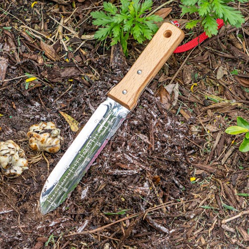 Nisaku Limited Edition Stainless Steel Weeding Knife with a 7.25-inch blade and inch markings laying on the gorund.