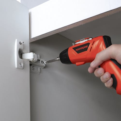 Person using the cordless screwdriver to install a hinge for a cabinet door.