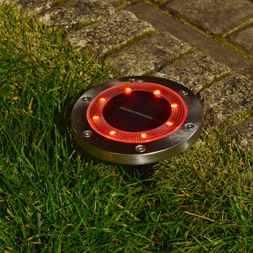 Metal disc pathway light staked in the ground with the red light.