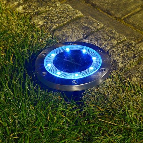 Metal disc pathway light staked in the ground with the blue light.