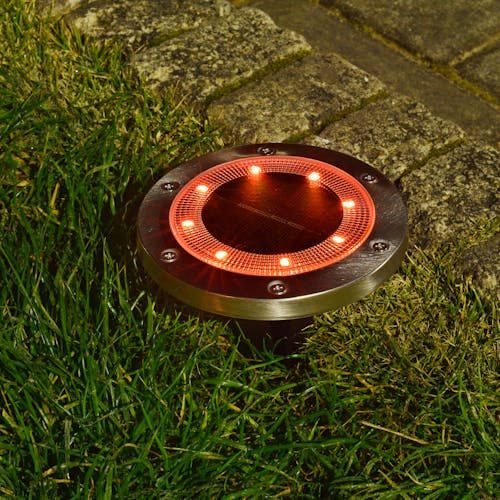 Metal disc pathway light staked in the ground with the orange light.