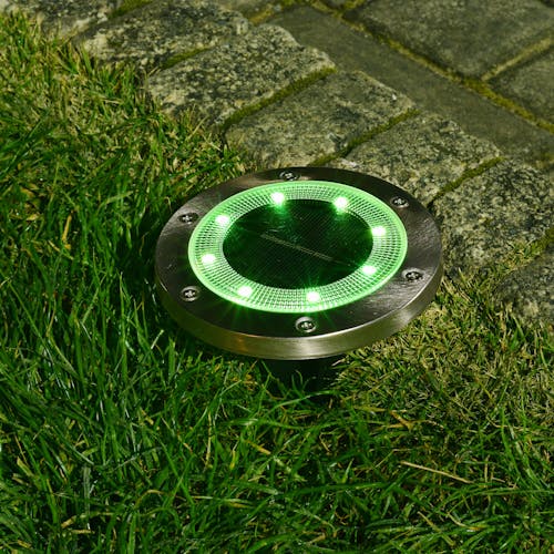 Metal disc pathway light staked in the ground with the green light.