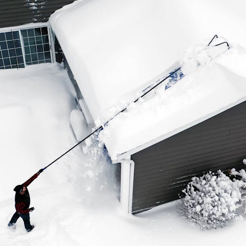Person reaching the top of their roof with the Snow Joe 28-foot snow removal roof rake with a 20-foot debris slide.
