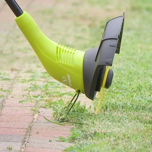 Sun Joe 4.5-amp 11.5-inch Electric 2-in-1 Stringless Grass Trimmer and Edger cutting the edge of a lawn.