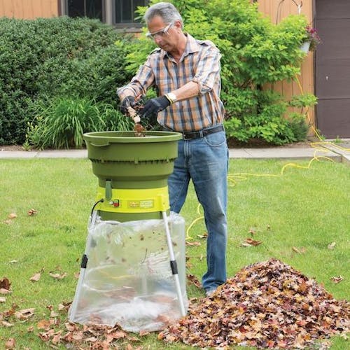Man dropping leaves into the Sun Joe 13-amp Electric Leaf Mulcher and Shredder outside on a front lawn.