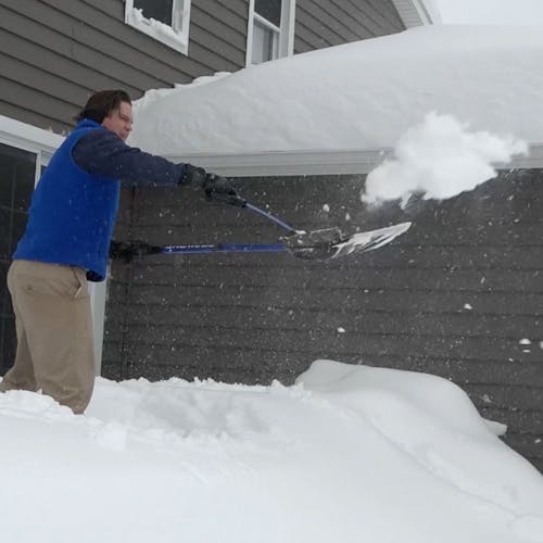 Snow Joe 18-inch Blue Shovelution Strain-Reducing Snow Shovel with spring assisted handle being used to throw snow away form a house.