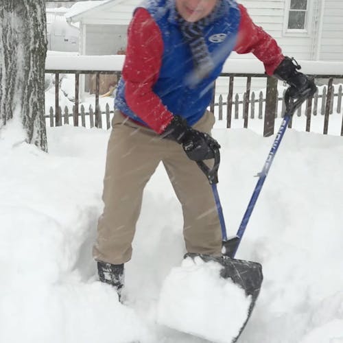 Snow Joe 18-inch Blue Shovelution Strain-Reducing Snow Shovel with spring assisted handle being used to throw snow off a patio deck.